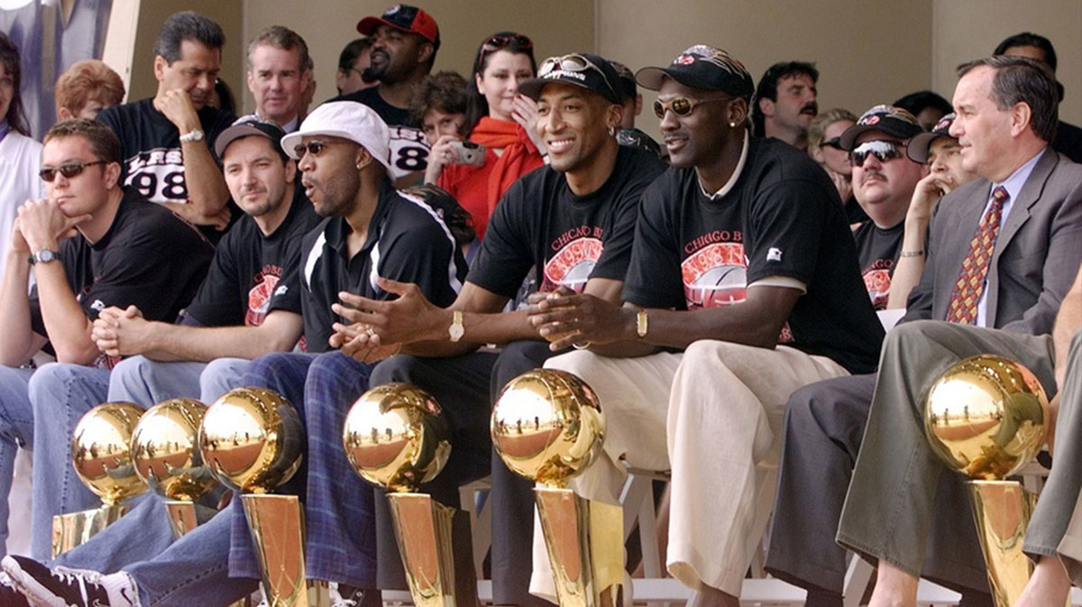 Chicago Bulls with their six championship trophies. Left to right in the front row are Luc Longley, Toni Kukoc, Ron Harper, Dennis Rodman (leaning back), Scottie Pippen, Michael Jordan and Chicago Mayor Richard Daley at a championship rally at Grant Park in Chicago.