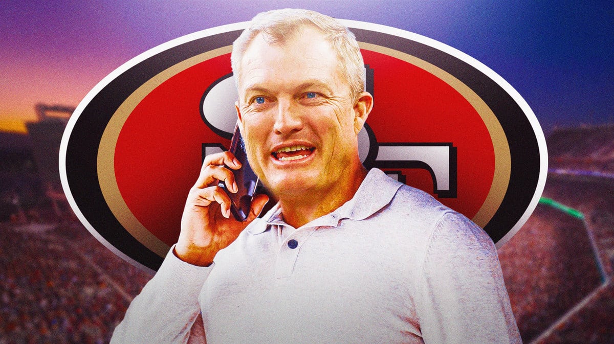 John Lynch talking on a cell phone with the 49ers logo in the background
