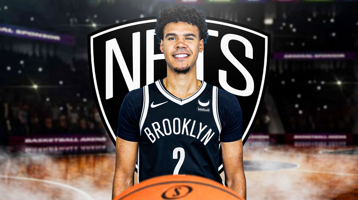 Image: Cam Johnson in middle of image looking happy, Brooklyn Nets logo, basketball court in background