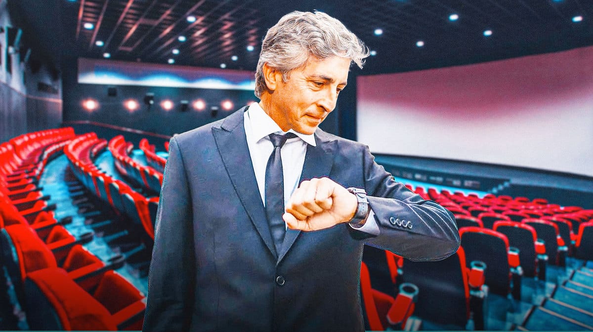 Director Alexander Payne looking at his watch in a movie theater with blank screen behind him.
