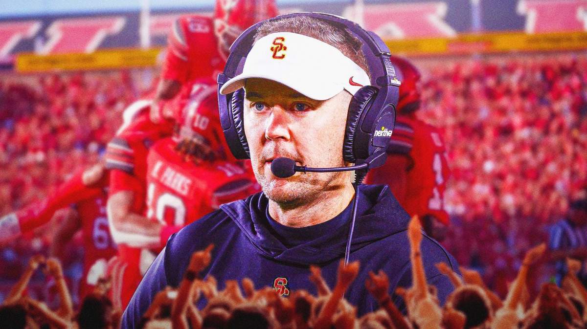 USC football coach Lincoln Riley looking solemn while Utah players celebrate in the background.