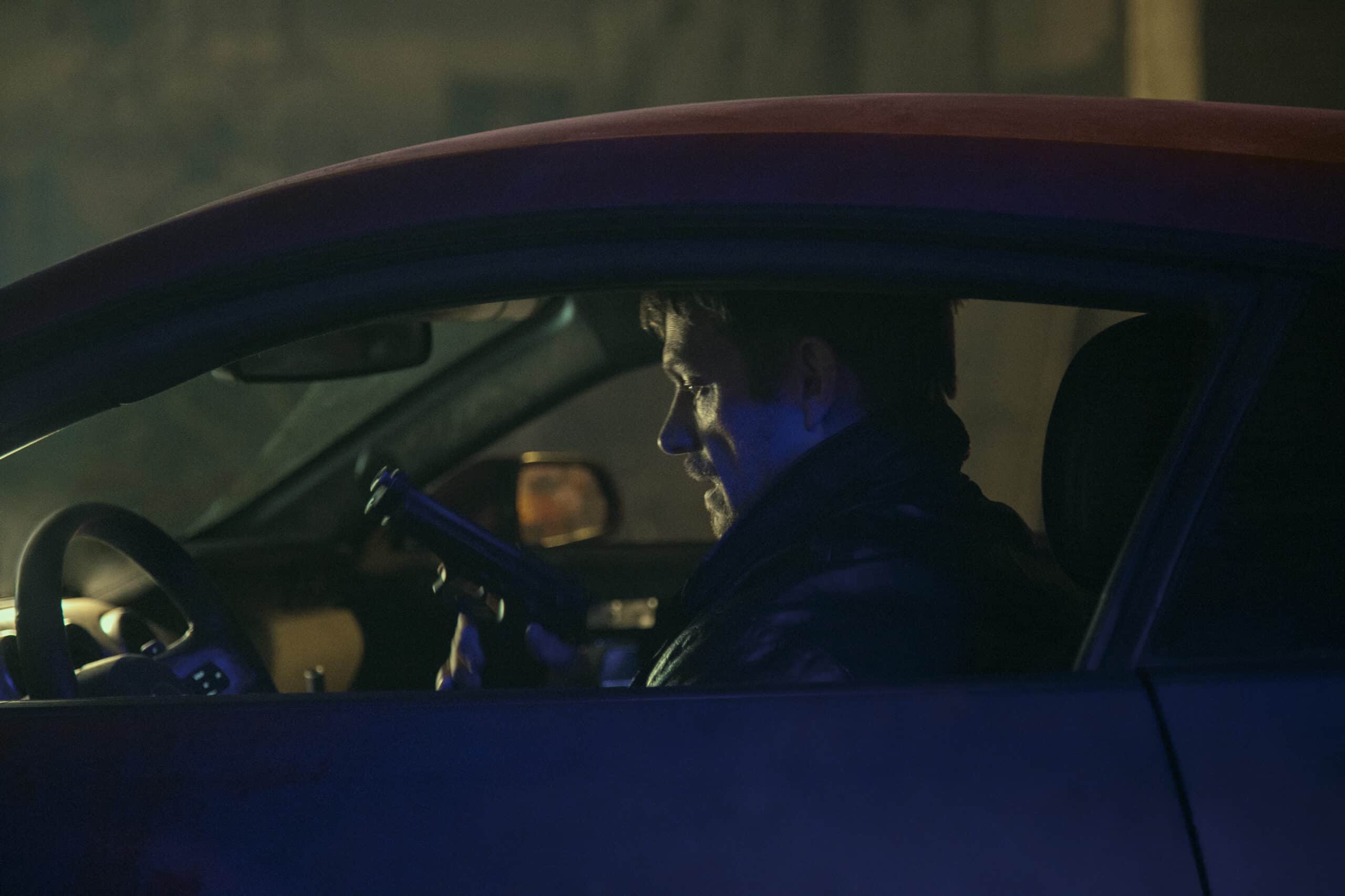 Joel Kinnaman in a car with a gun.