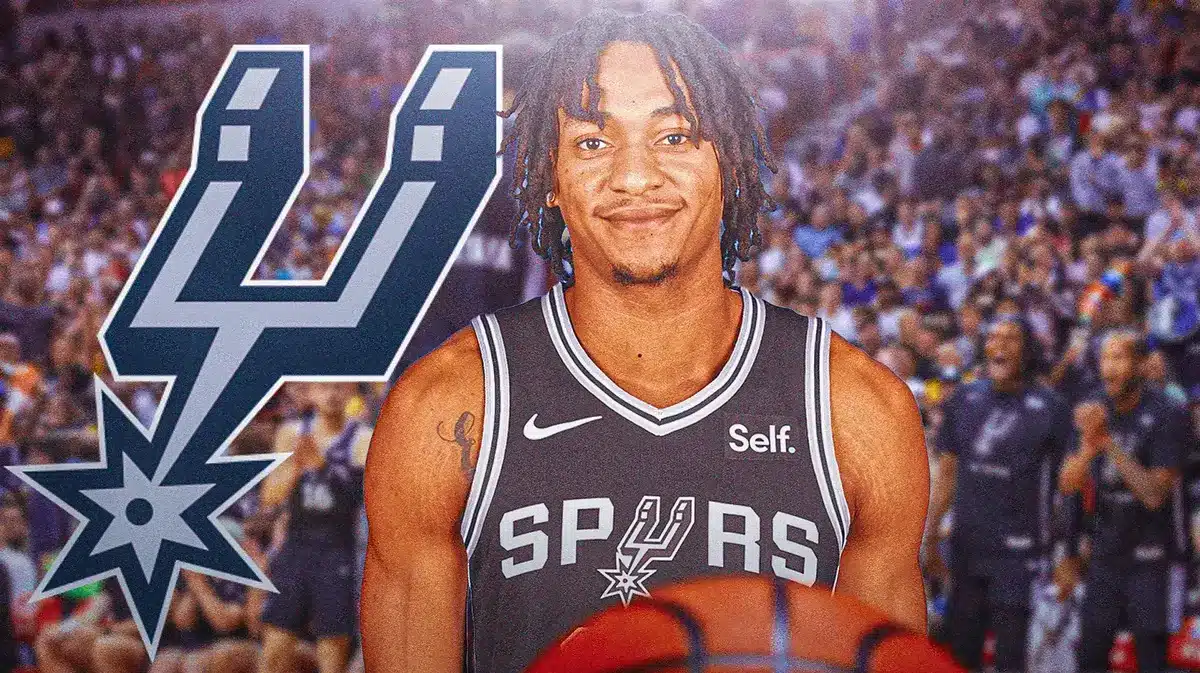 Devin Vassell in middle of image looking happy, SA Spurs logo, basketball court in background