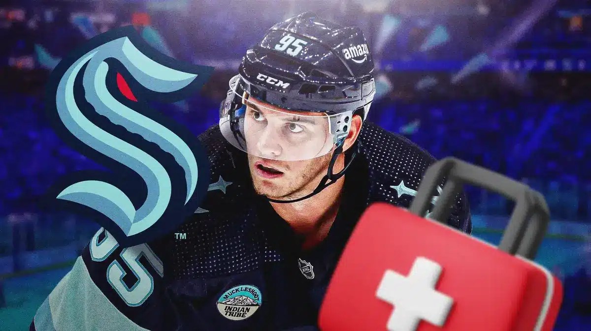Andre Burakovsky in middle of image looking stern, first aid kit, SEA Kraken logo, hockey rink in background