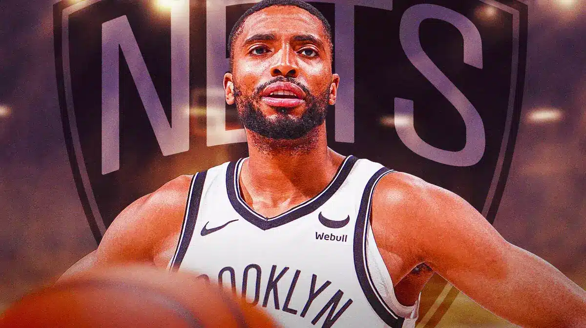 Mikal Bridges in middle of image looking stern, BK Nets logo, basketball court in background
