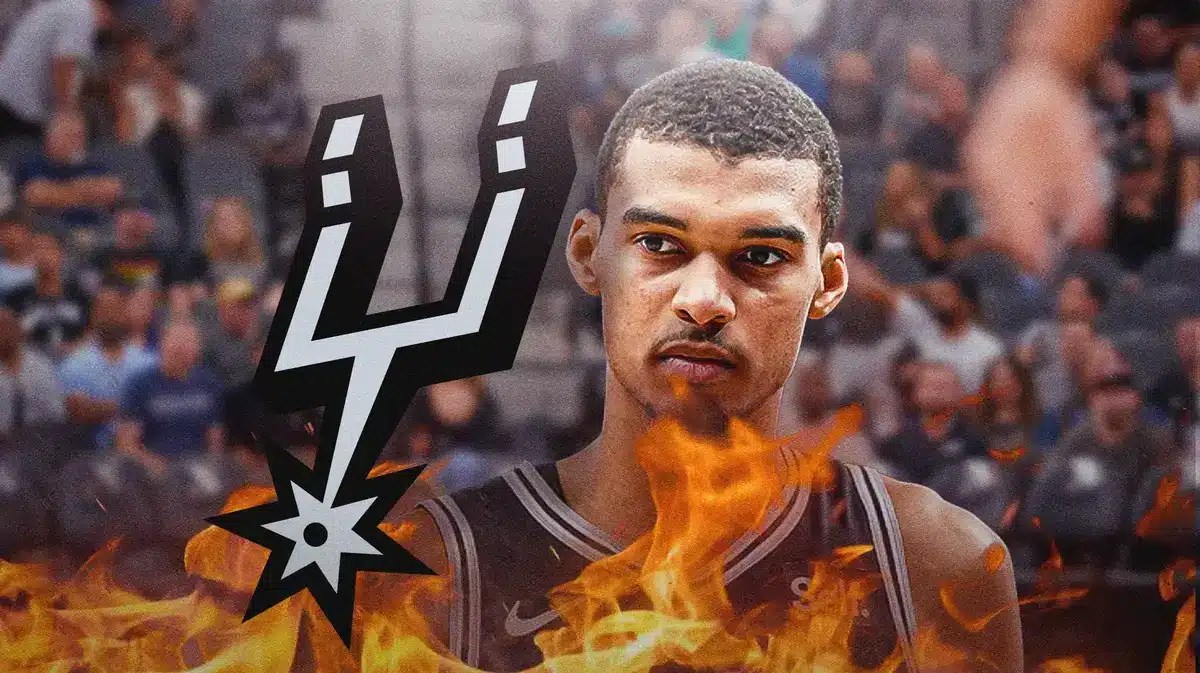 Victor Wembanyama in middle of image looking stern but with fire around him, SA Spurs logo, basketball court in background