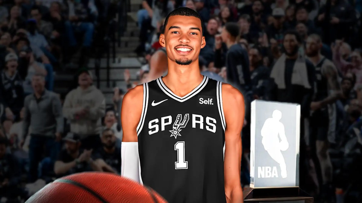 Victor Wembanyama alongside the NBA's Rookie of the Year trophy and with the Spurs arena in the background