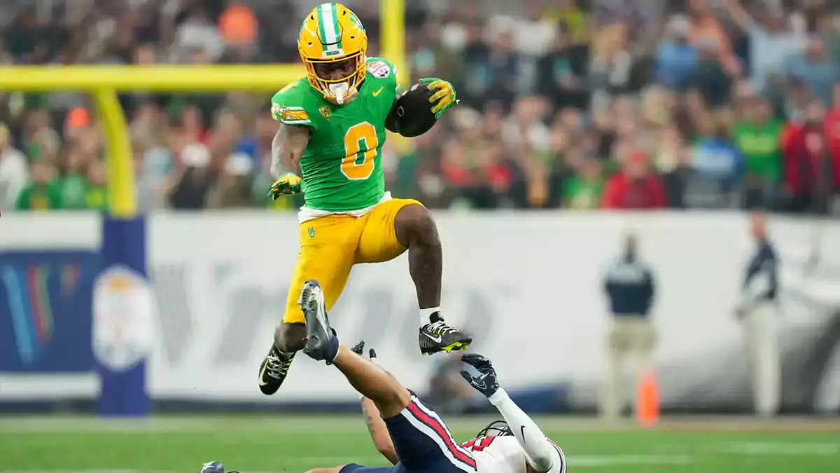  Oregon Ducks running back Bucky Irving (0) hurdles over Liberty Flames defensive back Brandon Bishop (6) during the second half in the 2024 Fiesta Bowl at State Farm Stadium