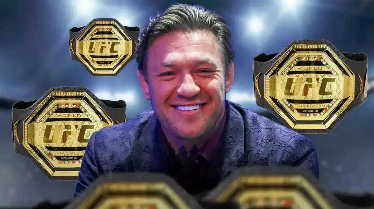 Conor McGregor smiling behind 3 UFC belts