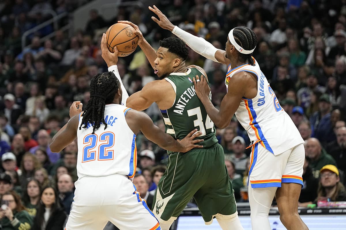 Milwaukee Bucks forward Giannis Antetokounmpo (34) holds the ball away from Oklahoma City Thunder guard Cason Wallace (22) and guard Shai Gilgeous-Alexander (2) during the third quarter at Fiserv Forum. 