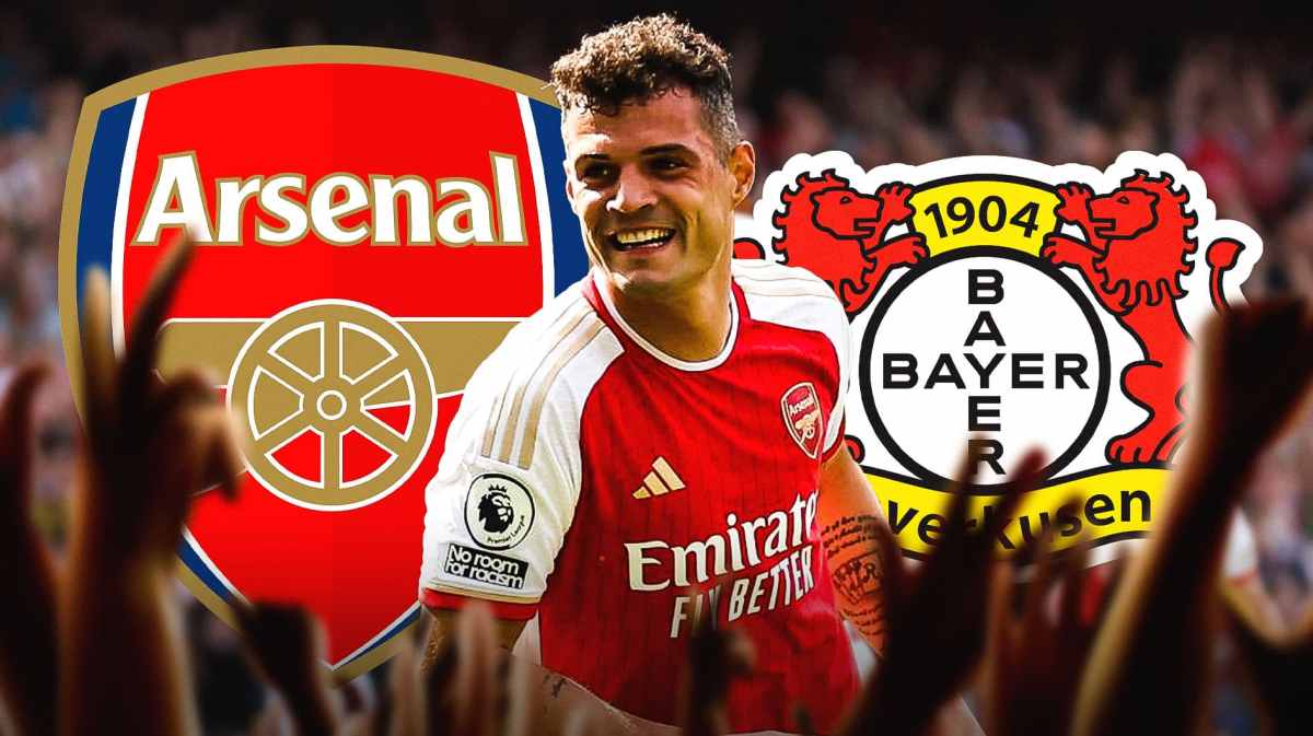 Granit Xhaka laughing in front of the Arsenal and Bayer Leverkusen logos