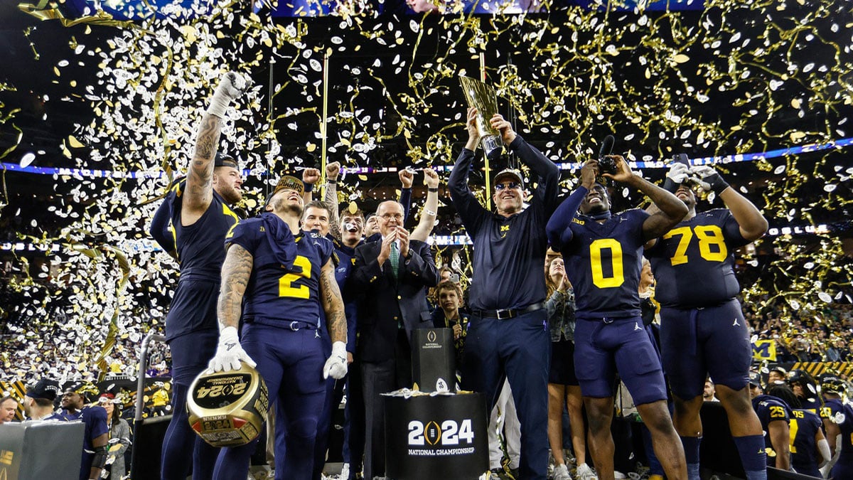 Michigan head coach Jim Harbaugh lifts up the trophy as players and coaches celebrate on stage after the 34-13 win over Washington to take the national championship game at NRG Stadium