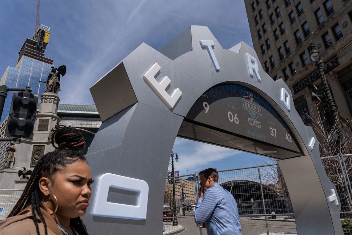 People walk past the countdown clock as work continues on the setup for the NFL draft near Campus Martius in downtown Detroit on April 16, 2024.