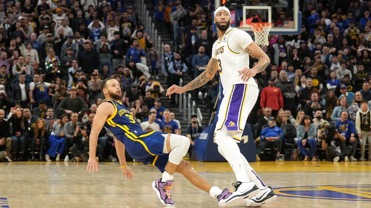 Golden State Warriors guard Stephen Curry (left) falls to the ground after shooting a three point basket against Los Angeles Lakers forward Anthony Davis (right) during the second overtime at Chase Center