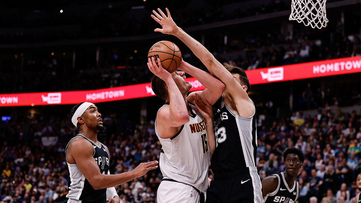 Denver Nuggets center Nikola Jokic (15) is fouled by San Antonio Spurs forward Zach Collins (23) as guard Devonte' Graham (4) defends in the third quarter at Ball Arena.