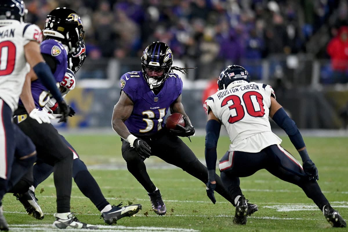Baltimore Ravens running back Dalvin Cook (31) runs the ball against Houston Texans linebacker Blake Cashman (53) and safety DeAndre Houston-Carson (30) during the fourth quarter of a 2024 AFC divisional round game at M&T Bank Stadium