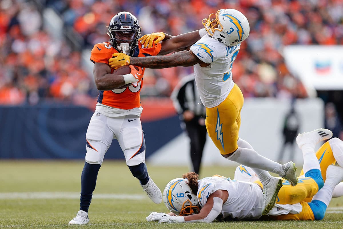 Denver Broncos running back Javonte Williams (33) stiff arms Los Angeles Chargers safety Derwin James Jr. (3) as linebacker Eric Kendricks (6) slides on the ground