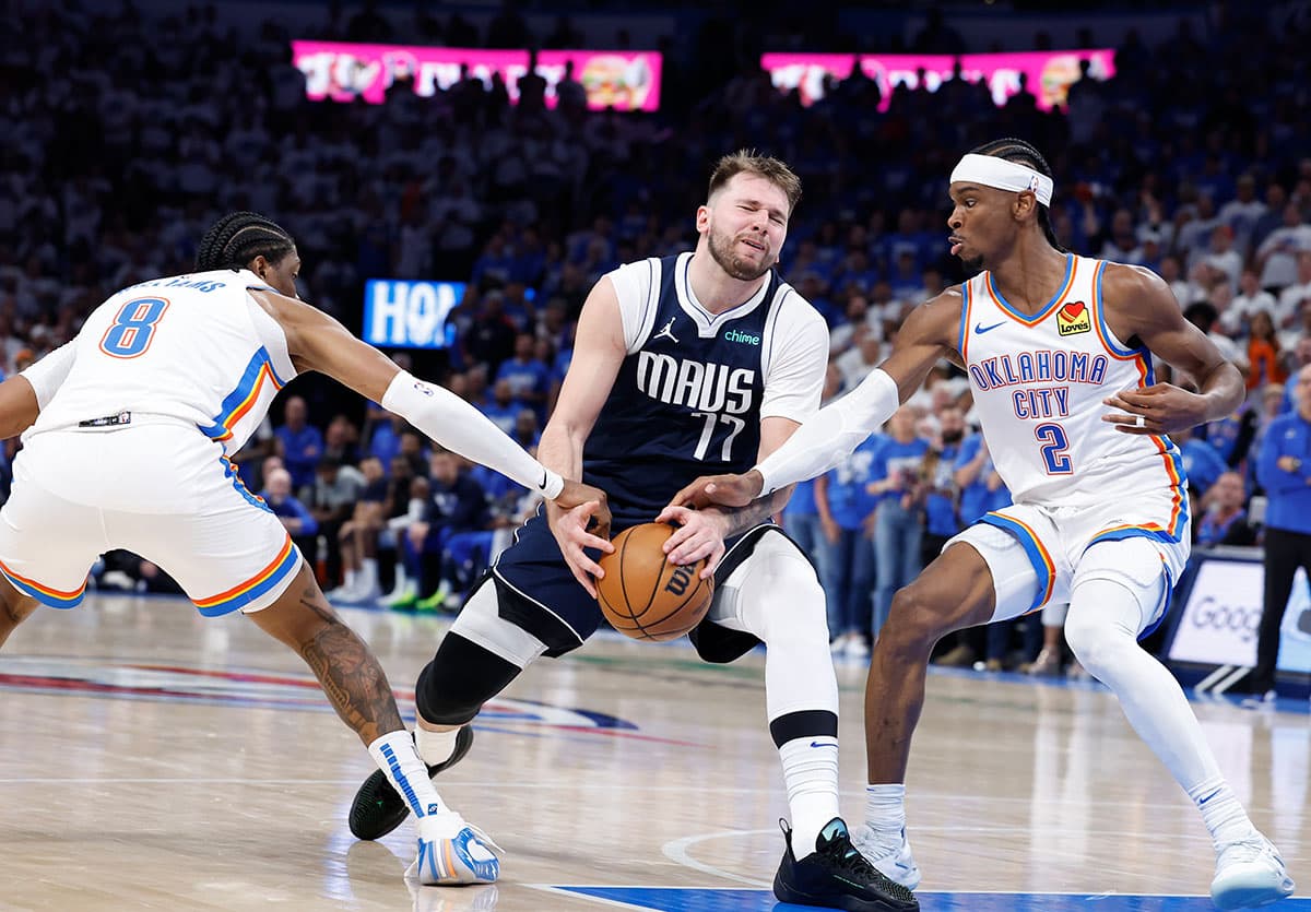Dallas Mavericks guard Luka Doncic (77) has the ball stripped as he drives between Oklahoma City Thunder guard Shai Gilgeous-Alexander (2) and forward Jalen Williams (8) during the second half of game one of the second round for the 2024 NBA playoffs at Paycom Center. 