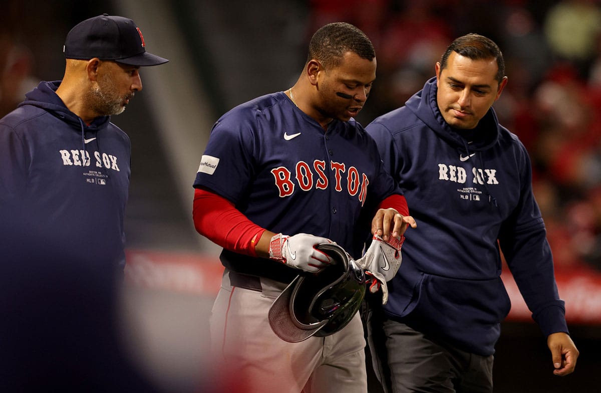 Boston Red Sox third baseman Rafael Devers (11) is checked by manager Alex Cora (left) and a trainer after being hit by a pitch during the sixth inning against the Los Angeles Angels at Angel Stadium.