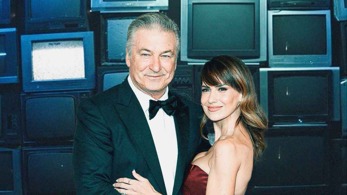 Alec Baldwin and Hilaria Baldwin with tvs behind him.