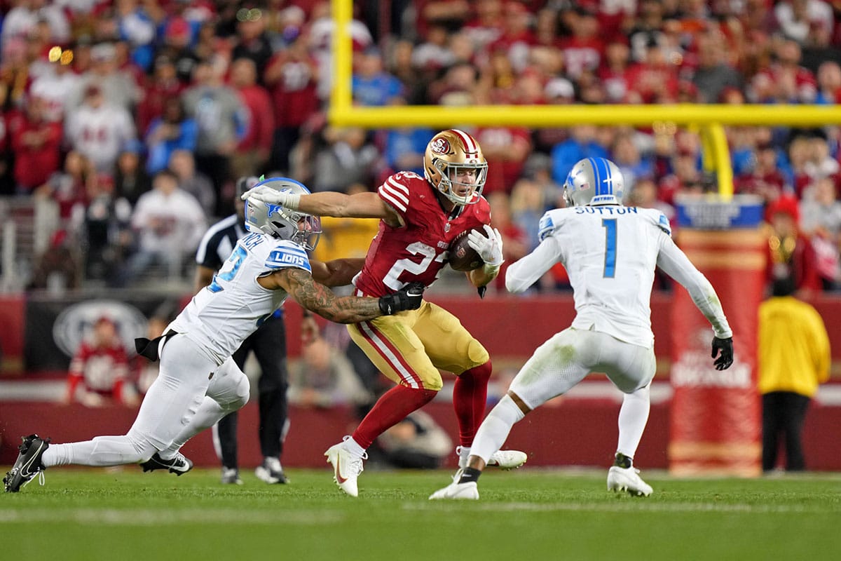 San Francisco 49ers running back Christian McCaffrey (23) runs with the ball against Detroit Lions safety Brian Branch (32) and cornerback Cameron Sutton (1) during the second half of the NFC Championship football game at Levi's Stadium.