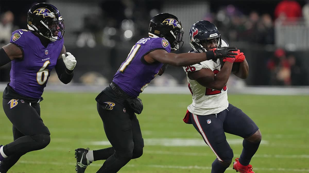 Houston Texans running back Devin Singletary (26) runs the ball against Baltimore Ravens linebacker Patrick Queen (6) and cornerback Brandon Stephens (21) during the third quarter of a 2024 AFC divisional round game at M&T Bank Stadium. 