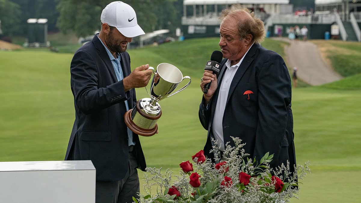 Jun 23, 2024; Cromwell, Connecticut, USA; Scottie Scheffler looks at the inscription on the Travelers Championship Trophy while speaking with Chris Berman during the final round of the Travelers Championship golf tournament at TPC River Highlands. Mandatory Credit: Gregory Fisher-USA TODAY Sports