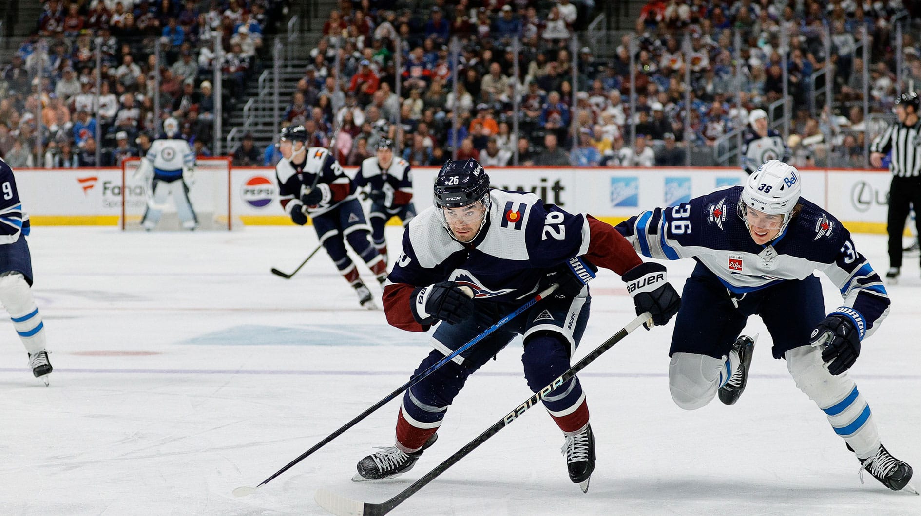 Colorado Avalanche defenseman Sean Walker (26) and Winnipeg Jets center Morgan Barron (36) chases down a loose puck in the first period at Ball Arena.