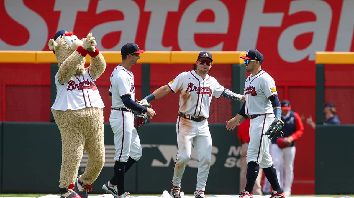 Atlanta Braves left fielder Eli White (36) and center fielder Jarred Kelenic (24) and right fielder Adam Duvall (14) celebrate after a victory as mascot Blooper looks on against the Philadelphia Phillies at Truist Park.