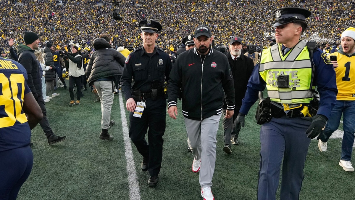 As fans rush the field, Ohio State Buckeyes head coach Ryan Day is escorted off the field following the NCAA football game against the Michigan Wolverines at Michigan Stadium. Ohio State lost 30-24.