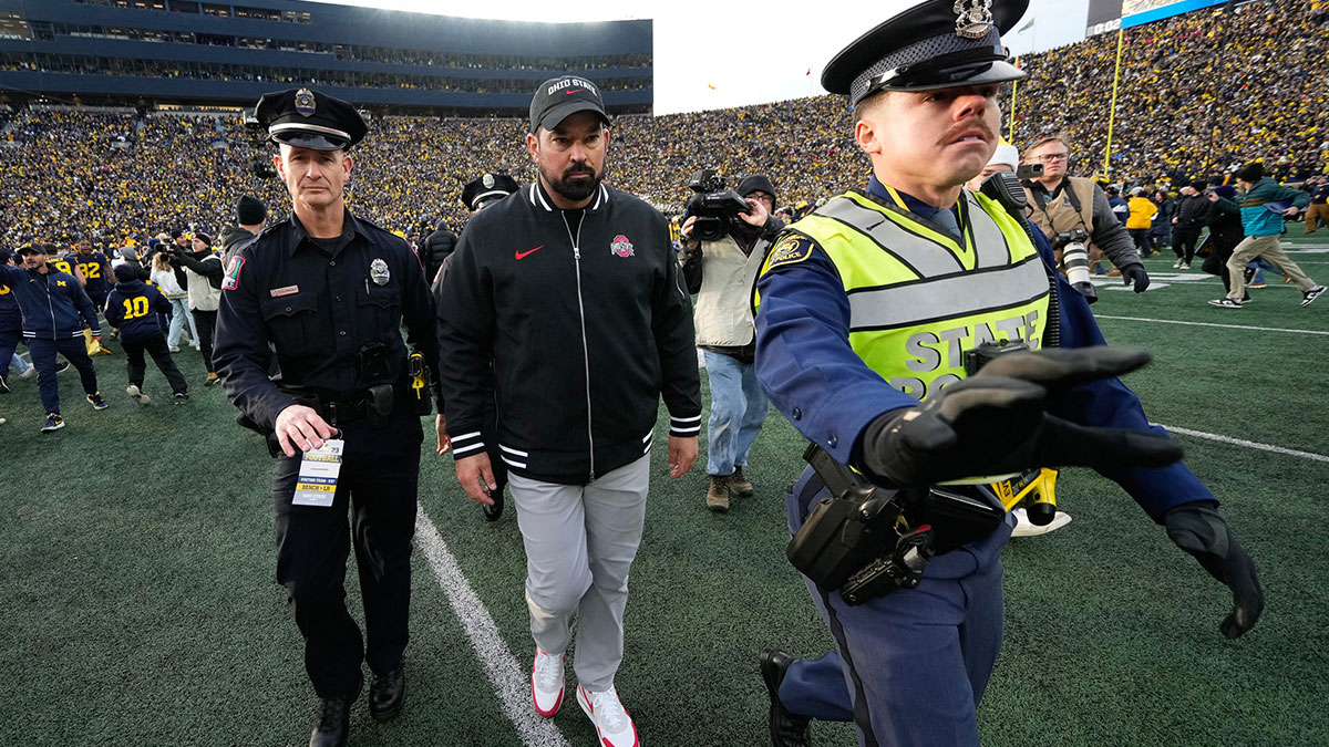 As fans rush the field, Ohio State Buckeyes head coach Ryan Day is escorted off the field following the NCAA football game against the Michigan Wolverines at Michigan Stadium. Ohio State lost 30-24.