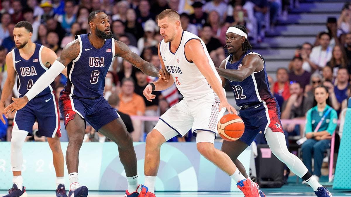 Serbia power forward Nikola Jokic (15) dribbles against United States guard Lebron James (6) and guard Jrue Holiday (12) in the first quarter during the Paris 2024 Olympic Summer Games at Stade Pierre-Mauroy. 