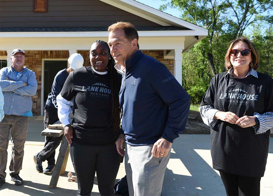 New homeowner Jinaka Chambers smiles as Nick and Terry Saban speak in front of her new home, the LANK House, a tribute to the 2023 Crimson Tide football team, funded by the Nick’s Kids Foundation for Habitat for Humanity.