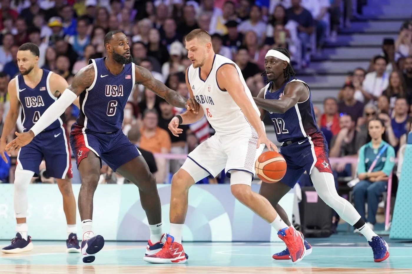 Serbia power forward Nikola Jokic (15) dribbles against United States guard Lebron James (6) and guard Jrue Holiday (12) in the first quarter during the Paris 2024 Olympic Summer Games at Stade Pierre-Mauroy.