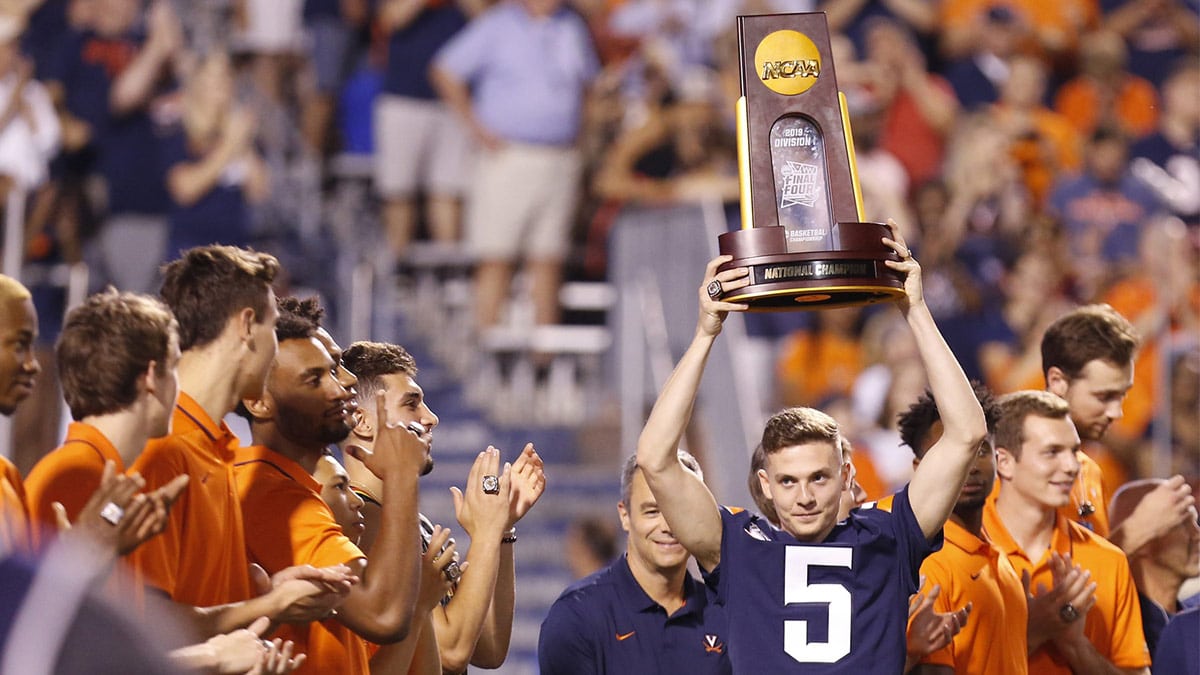 Former Virginia Cavaliers basketball player Kyle Guy holds the 2019 national championship trophy during a ceremony recognizing the national champion Cavaliers at the end of the first quarter of the Cavaliers game against the Florida State Seminoles at Scott Stadium.