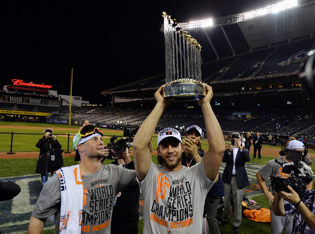 San Francisco Giants starting pitcher Ryan Vogelsong (left) watches as teammate Madison Bumgarner (middle) hoists the Commissioners Trophy after game seven of the 2014 World Series against the Kansas City Royals at Kauffman Stadium.