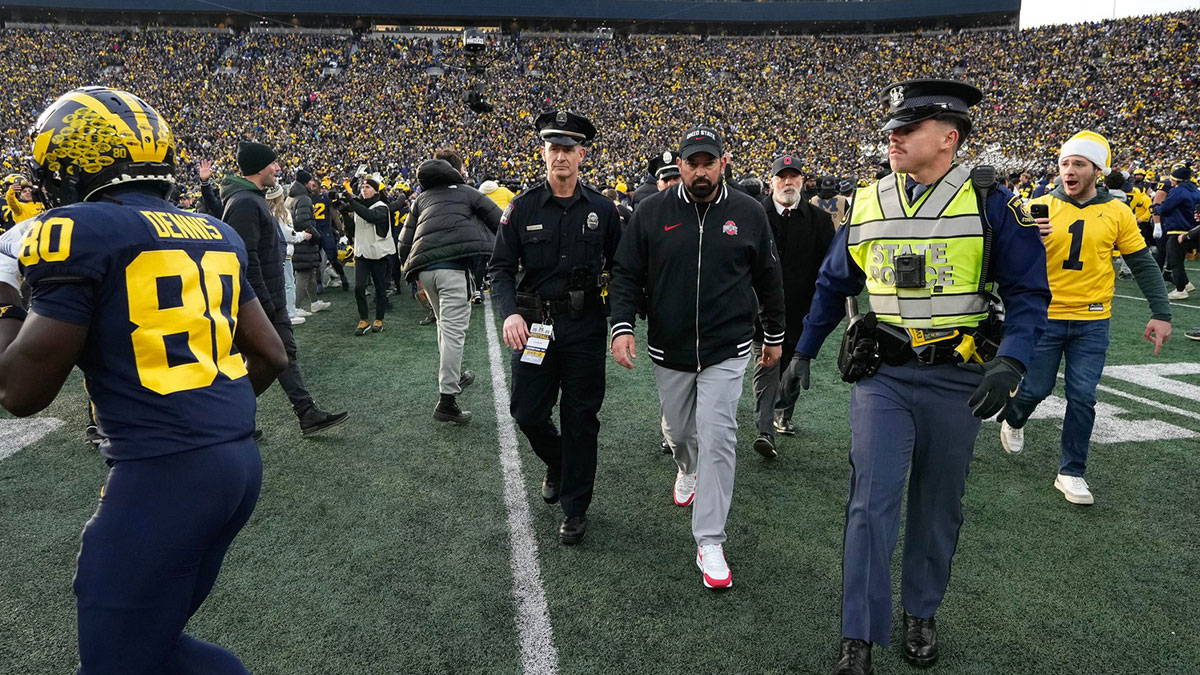 As fans rush the field, Ohio State Buckeyes head coach Ryan Day is escorted off the field following the NCAA football game against the Michigan Wolverines at Michigan Stadium. Ohio State lost 30-24.