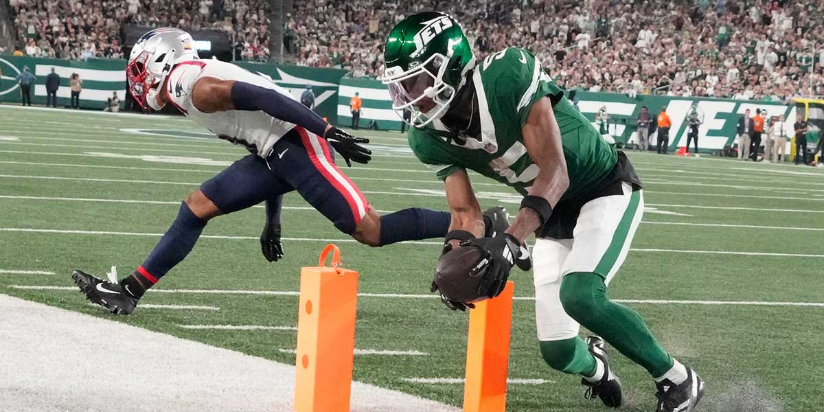 Sep 19, 2024; East Rutherford, New Jersey, USA; New York Jets wide receiver Garrett Wilson (5) scores a 3rd quarter touchdown in front of New England Patriots cornerback Christian Gonzalez (0) at MetLife Stadium. Mandatory Credit: Robert Deutsch-Imagn Images