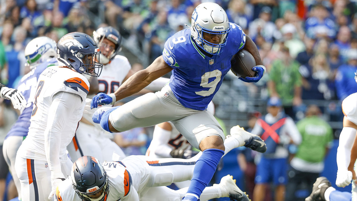 Sep 8, 2024; Seattle, Washington, USA; Seattle Seahawks running back Kenneth Walker III (9) jumps over a tackle attempt by Denver Broncos cornerback JaQuan McMillian (29) during the second quarter at Lumen Field. 