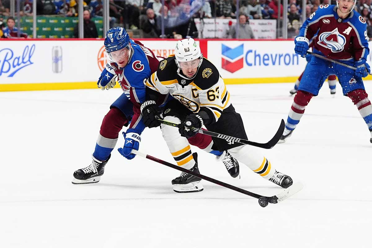 Colorado Avalanche defenseman Cale Makar (8) pokes the puck away from Boston Bruins left wing Brad Marchand (63) in the third period at Ball Arena.