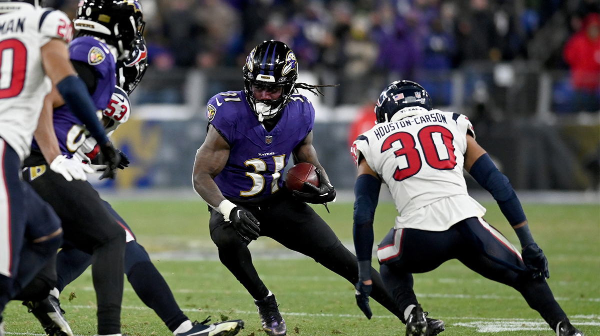 Baltimore Ravens running back Dalvin Cook (31) runs the ball against Houston Texans linebacker Blake Cashman (53) and safety DeAndre Houston-Carson (30) during the fourth quarter of a 2024 AFC divisional round game at M&T Bank Stadium.