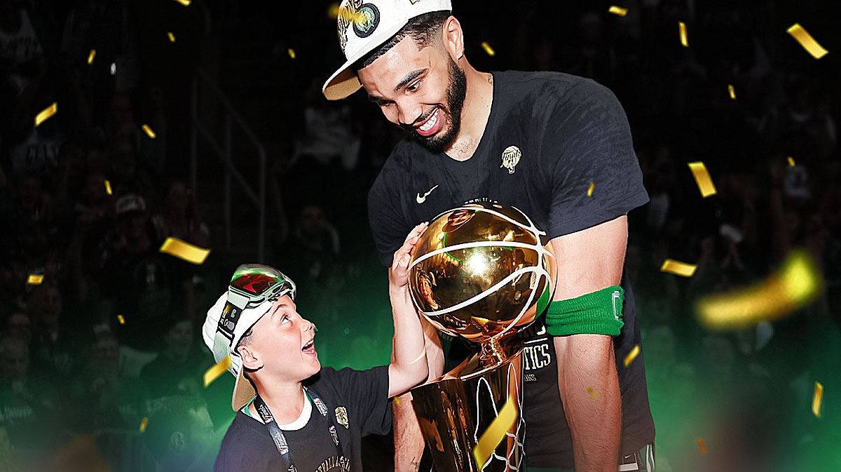 Jayson Tatum in Celtics uniform with son Deuce next to Finals trophy.