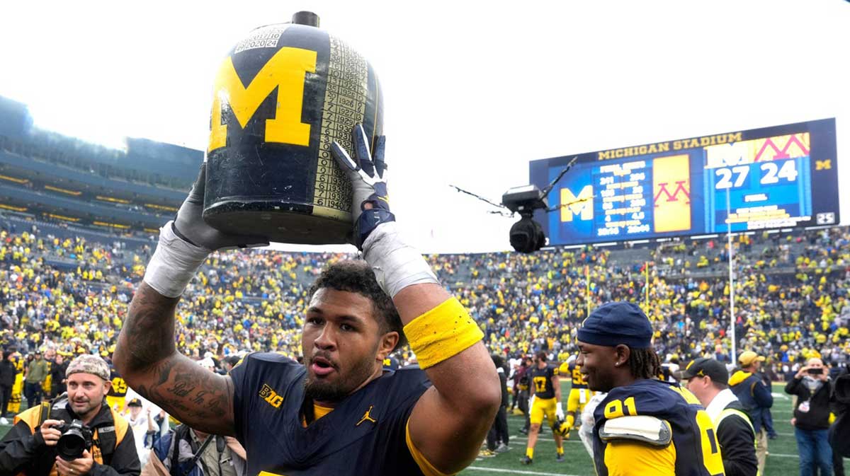 Michigan defensive end TJ Guy holds up the Little Brown Jug as he heads towards the student section after the team's 27-24 win over Minnesota at Michigan Stadium