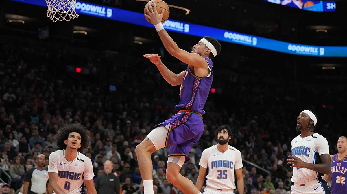 Phoenix Suns guard Devin Booker (1) scores a basket in between Orlando Magic guard Anthony Black (0), center Goga Bitadze (35), and guard Jalen Suggs (4) during the first half of an NBA game at Footprint Center.