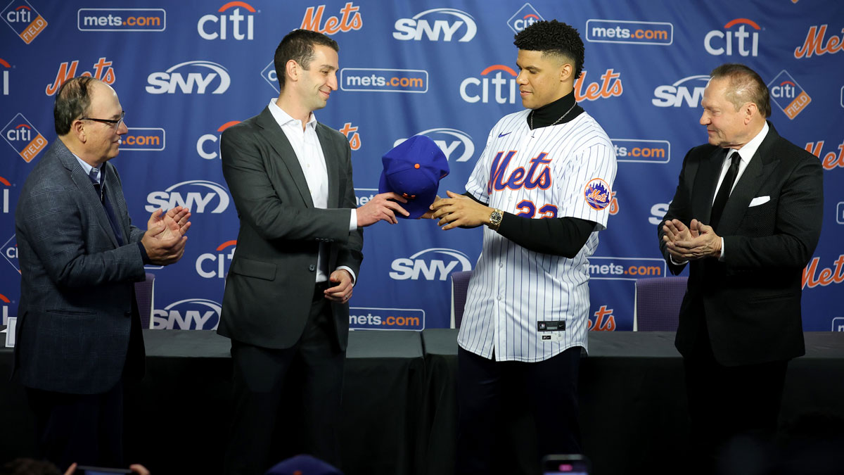 New York Mets general manager David Stearns hands a cap to New York Mets right fielder Juan Soto (22) during Soto's introductory press conference at Citi Field. Also pictured New York Mets owner Steve Cohen (left) and agent Scott Boras (right)