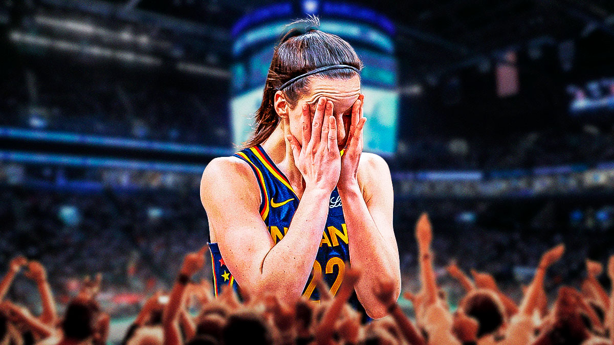 Fever guard Caitlin Clark in pain, holding her ear, and a background of Barclays Center with the New York Liberty fanbase in the background