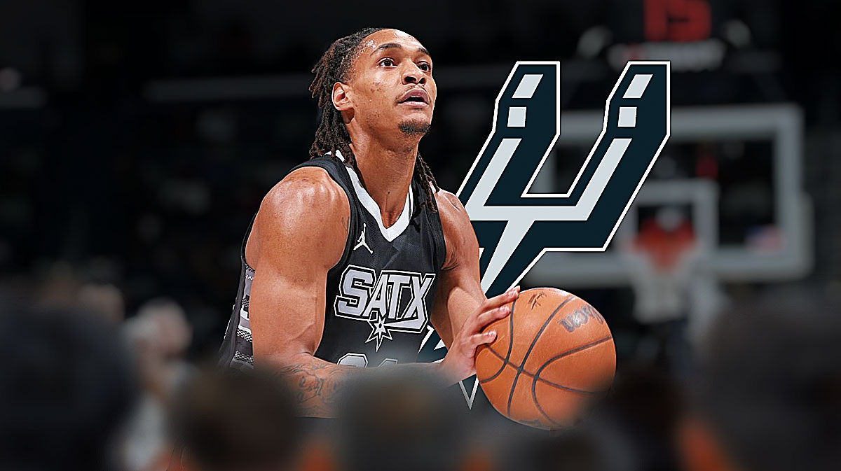 Devin Vassell looking content, Spurs logo, a basketball/rim image in the background