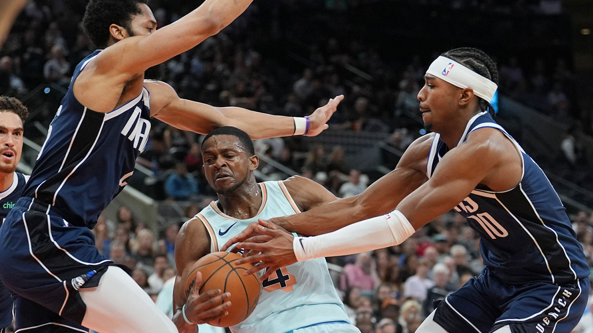 圣安东尼奥马刺后卫De'aaron Fox（4）在上半场在弗罗斯特银行中心对阵达拉斯小牛队的球员Spencer Dinwiddie（26岁）和Brandon Williams（10）。 