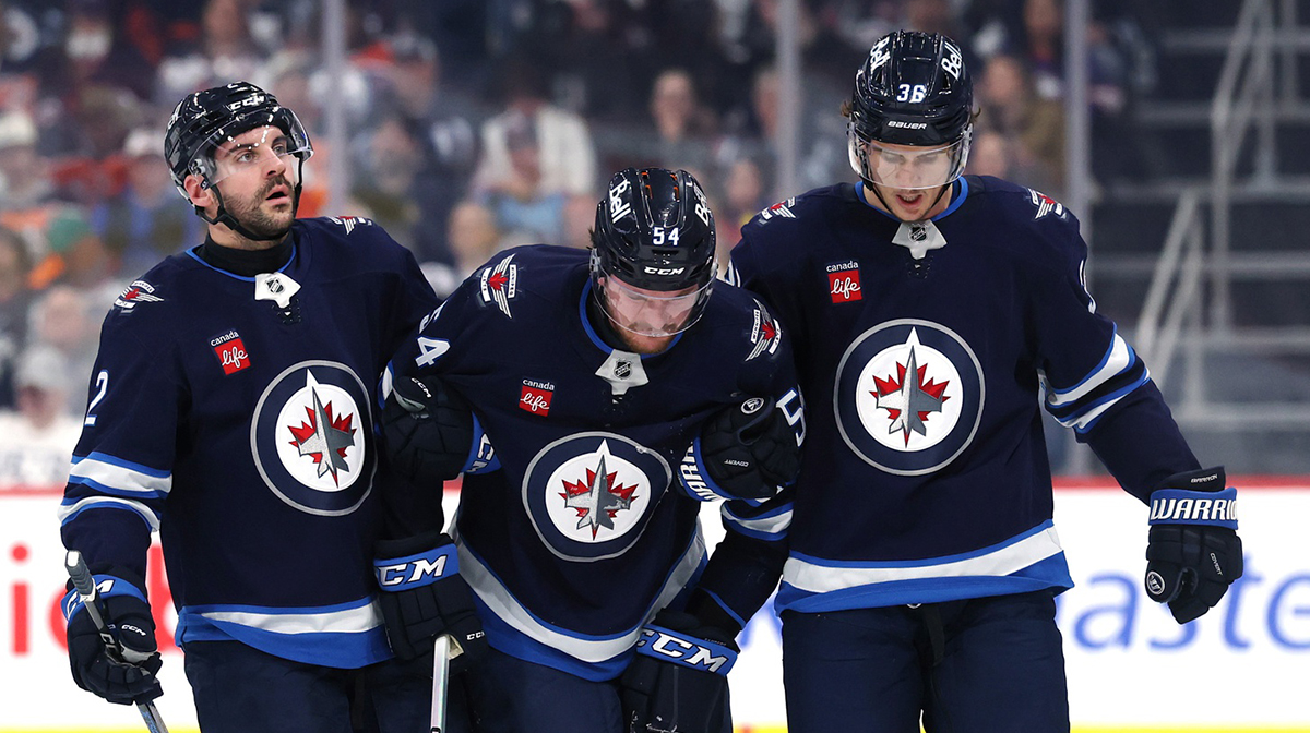An injured Winnipeg Jets defenseman Dylan Samberg (54) is taken of the ice during a game against the Edmonton Oilers with the help of Winnipeg Jets defenseman Dylan DeMelo (2) and Winnipeg Jets center Morgan Barron (36) in the second period at Canada Life Centre.