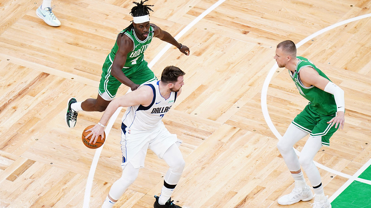 Dallas Mavericks guard Luka Doncic (77) controls the ball against Boston Celtics guard Jrue Holiday (4) and center Kristaps Porzingis (8) in the first quarter during game five of the 2024 NBA Finals at TD Garden.